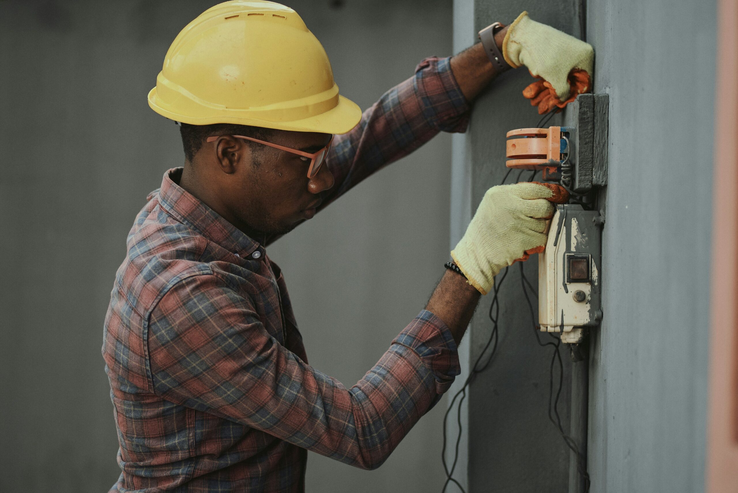 Skilled electrician in a yellow hard hat working on an electrical panel